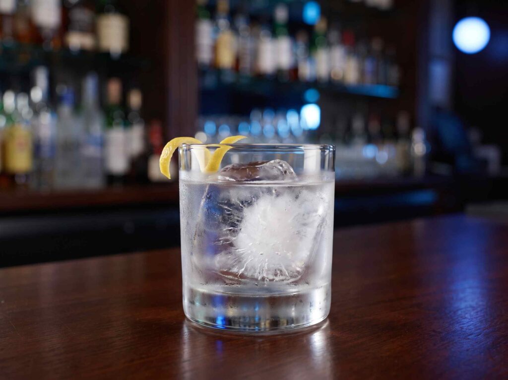 Glass of vodka served neat over a large ice cube with lemon peel